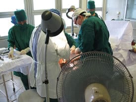 Cooled by a fan, UAMS surgeon Ruth Thomas, M.D., at right in the dark scrubs, works in a humid Vietnamese operating room.