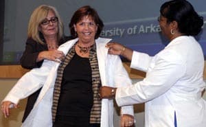 Dr. Susan Moss-Logan (left) and Dr. Betholyn Gentry (right) put a white coat on Julie Beard, who earned a Ph.D. in Communication Science and Disorders.