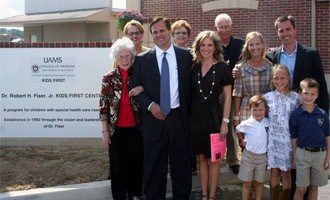 Members of the Fiser family stand next to the sign dedicating the facility to the late Robert Fiser Jr., M.D., a champion of the KIDS FIRST program and a Morrilton native.