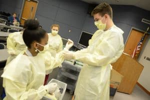 Students help one another put on surgical gloves.