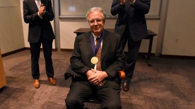 Martin Hauer-Jensen, M.D., Ph.D., is presented with a chair as part of the investiture ceremony, while College of Pharmacy Dean Keith M. Olsen, Pharm.D., and Chancellor Dan Rahn, M.D., look on.