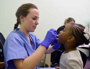 Ashley McMillan, D.M.D., assistant director of the Oral Health Clinic and General Practice Residency Program at UAMS, checks a young girl for cavities during an oral health screening at the Davis Head Start center.
