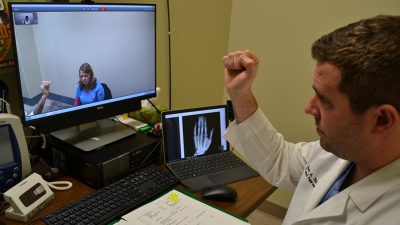 Orthopaedic surgeon Mark Tait, M.D., via a live video connection demonstrates to an Arkansas Department of Corrections inmate patient and a prison nurse how Tait wants him to make a fist as part of a medical examination.