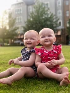 Twin babies smiling while sitting on a lawn