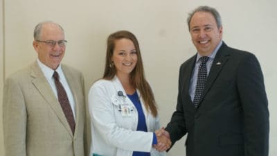Third-year medical student Zoe Weeks (center), flanked by UAMS College of Medicine Dean Christopher T. Westfall, M.D., shakes hands with Corey Little, president of Arkansas Mutual Insurance Co.