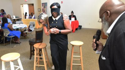 Kenneth O. Young, right, watches as Leanne Lefler guides a blindfolded volunteer from the audience through an obstacle course at the FAITH Network Summit.