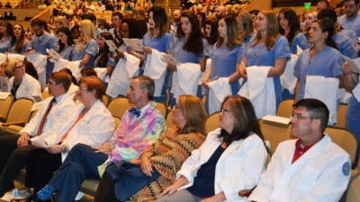 UAMS College of Nursing juniors stand and recite the Nightingale Pledge before putting on their white coats on stage.
