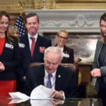 (From left) Arkansas Sen. Missy Irvin; UAMS Chancellor Cam Patterson, M.D., MBA; and Rep. Michelle Gray look on as Gov. Asa Hutchinson (seated) signs Senate Bill 151 in support of the UAMS Cancer Institute's quest for National Cancer Institute Designation.