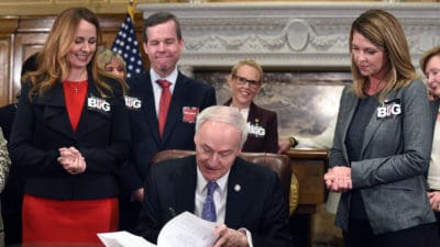 (From left) Arkansas Sen. Missy Irvin; UAMS Chancellor Cam Patterson, M.D., MBA; and Rep. Michelle Gray look on as Gov. Asa Hutchinson (seated) signs Senate Bill 151 in support of the UAMS Cancer Institute's quest for National Cancer Institute Designation.