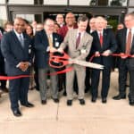 Mark Deal and Chancellor Cam Patterson use oversized scissors from the Pine Bluff Regional Chamber of Commerce for the official ribbon cutting at the South Central Regional Campus.