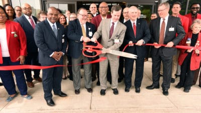 Mark Deal and Chancellor Cam Patterson use oversized scissors from the Pine Bluff Regional Chamber of Commerce for the official ribbon cutting at the South Central Regional Campus.
