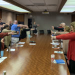 Employees from the UAMS Office of Communications and Marketing stretch during a team meeting.