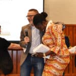 Jeff Standridge, center, embraces a tearful Selom Ayawovi Ametepe in celebration after the announcement that PAKI Solutions, Ametepe's team, had won the Boot Camp competition. Nancy Gray, left, shakes the hand of another team member.