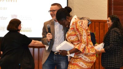 Jeff Standridge, center, embraces a tearful Selom Ayawovi Ametepe in celebration after the announcement that PAKI Solutions, Ametepe's team, had won the Boot Camp competition. Nancy Gray, left, shakes the hand of another team member.