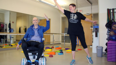 Two people, one in wheelchair, making big movements with arms