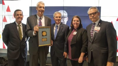 UAMS Chancellor Cam Patterson, M.D., MBA, Mahlon O. Maris, M.D., Curtis Barnett, Angela Wimmer, M.Ed., and Curtis Lowery, M.D., pose in front of a digital health interpretive wall commemorating the digital health partnership and honoring Maris' legacy.