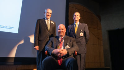 J.D. Day, M.D. (seated) wears his commemorative medallion from the investiture alongside UAMS College of Medicine Dean Christopher T. Westfall, M.D., FACS and UAMS Chancellor Cam Patterson, M.D., MBA.