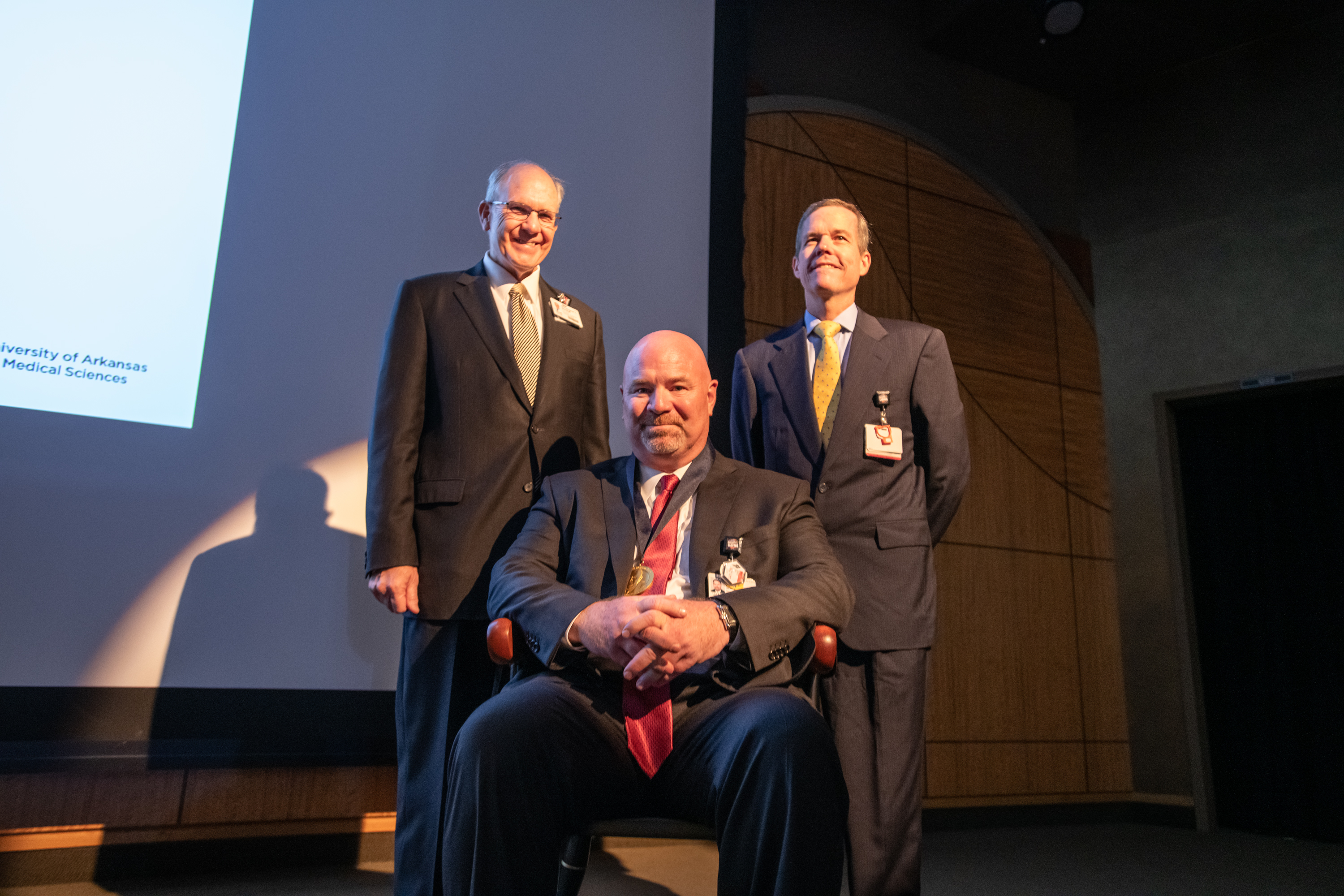 J.D. Day, M.D. (seated) wears his commemorative medallion from the investiture alongside UAMS College of Medicine Dean Christopher T. Westfall, M.D., FACS and UAMS Chancellor Cam Patterson, M.D., MBA.