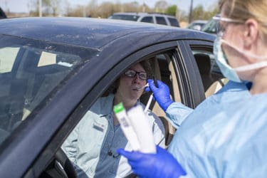 A patient, left, has her temperature taken while waiting in line in her car in Helena.