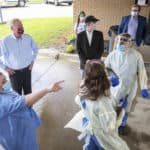 Jennifer Hunt, left, points toward the entryway for the drive-thru while describing the flow of traffic to Gov. Asa Hutchinson, second from left, and UAMS Chancellor Cam Patterson (wearing black cap).