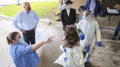 Jennifer Hunt, left, points toward the entryway for the drive-thru while describing the flow of traffic to Gov. Asa Hutchinson, second from left, and UAMS Chancellor Cam Patterson (wearing black cap).