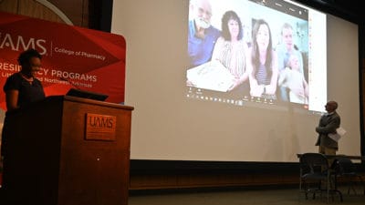 Kendrea Jones, Pharm.D., left, and Mark Granberry, Pharm.D., listen to graduating resident Julianne Mott as she speaks from her home via a live video connection.