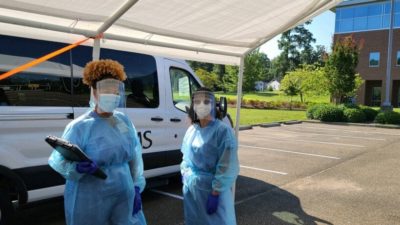 Dia Partlow, left, and Mariella Hernandez get ready to help with drive-up COVID-19 testing in Magnolia. The van behind them was purchased with money from a donation by Blue & You Foundation. Bank of America also recently donated money to support the Mobile Unit.
