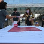 Students from the colleges of Public Health and Health Professions sign the diversity pledge banner, while faculty and staff greet them and help disinfect pens and markers.