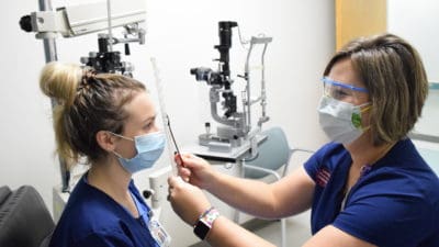 Alicia Baird, director of the Ophthalmic Medical Technology program and department chair, demonstrates how to perform a prism alternate cover test (PACT) on student Mallory England.