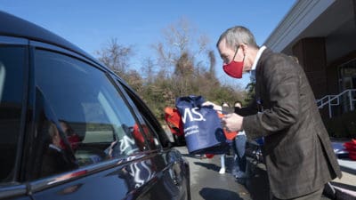 UAMS Chancellor Cam Patterson hands a large tote bag containing masks, hand sanitizer and bilingual information on Covid-19 during a drive-thru event Dec. 22 at Second Baptist Church in Little Rock.