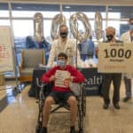 Michael Kent, seated left, holds a sign announcing he is the 1,000th COVID-19 patient to be discharged by the UAMS Medical Center. Behind Kent, left to right, are UAMS Chancellor Cam Patterson, UAMS Medical Center CEO Steppe Mette and hospitalist Franklin Gray.