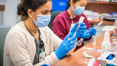 Pharmacist Neha Sharma, Pharm.D., and College of Pharmacy student Gabriella Nepomuceno work in the UAMS COVID-19 vaccination clinic. Starting Feb. 25, the clinic is relocating to the Centre at University Park at 6401 West 12th St., in Little Rock.