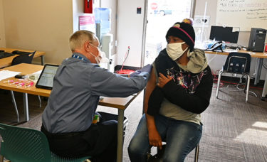 Robert Hopkins, M.D., left, finishes vaccinating a patient March 22 at the Jericho Way Day Resource Center in Little Rock.