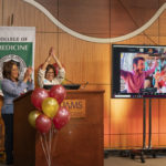 Madison Morris celebrates with family onscreen while Sharanda Williams and Sara Tariq, M.D., watch from the podium in the auditorium.