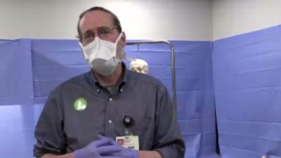 Kevin Phelan, Ph. D., talks to AHA Sweethearts as a medical resident waits on bed behind him to help him demonstrate an ultrasound.