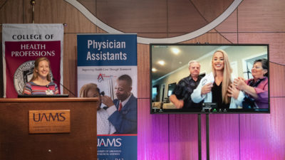 Tiffany Huitt, Ph.D., left, reads off the names of the 40 members of the Physician Assistant Class of 2023 as each in turn puts on their white coat during a partly virtual white coat ceremony.