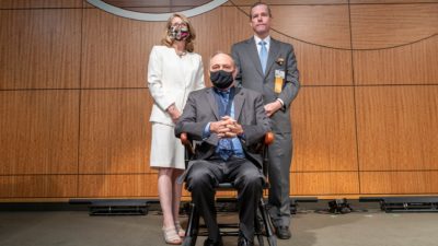 UAMS Executive Vice Chancellor and College of Medicine Dean Susan Smyth, M.D., and UAMS Chancellor Cam Patterson, M.D., MBA, present Birrer (seated) with his commemorative medallion and inscribed wooden chair.