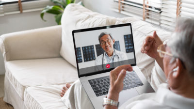 stock image of patient communicating with doctor via laptop from sofa