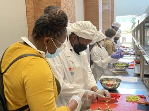 Katina White, educational coordinator for Pathways Academy, offers advice to a student chopping vegetables.