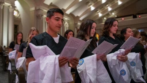 Students in the College of Nursing stand and read from their programs during the white coat ceremony.