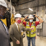 Little Rock Mayor Frank Scott, left, looks on as Chancellor Cam Patterson, center, prepares to push a button on a control panel to start one of the generators at the 2021 dedication of the new UAMS power plant on the east side of the Little Rock campus.