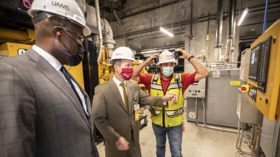 Little Rock Mayor Frank Scott, left, looks on as Chancellor Cam Patterson, center, prepares to push a button on a control panel to start one of the generators at the 2021 dedication of the new UAMS power plant on the east side of the Little Rock campus.