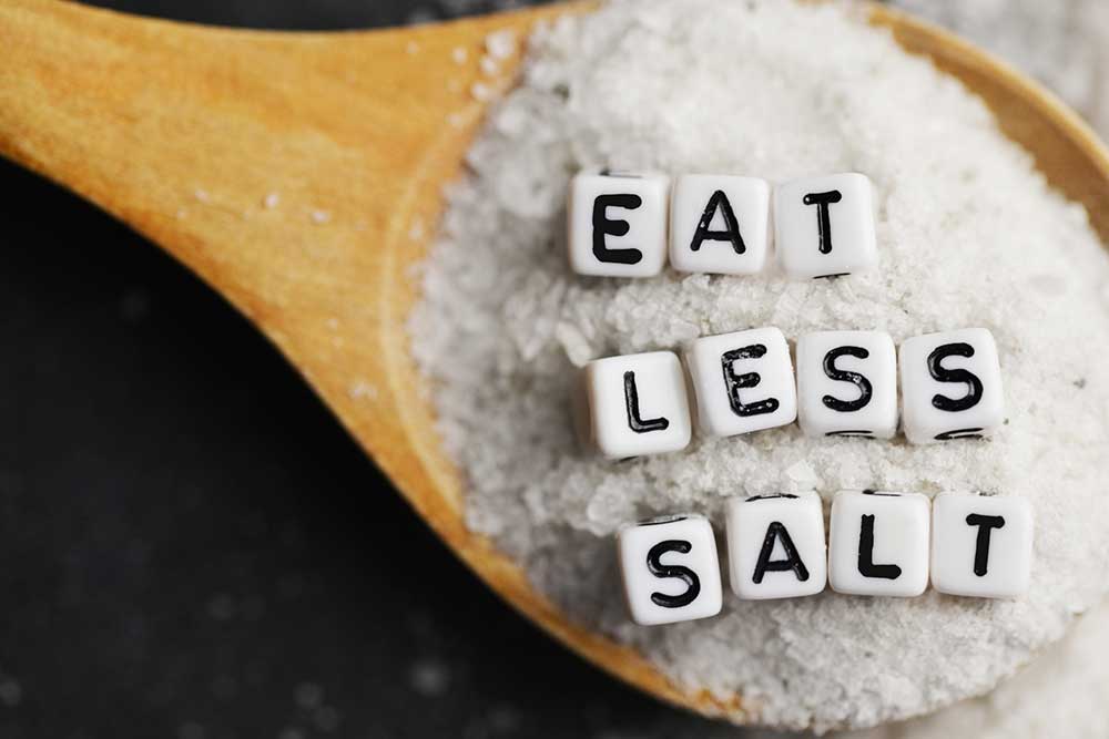 Salt in spoon with the words "Eat Less Salt"