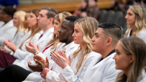 Graduate students wear their white coats as they sit during the College of Nursing ceremony.
