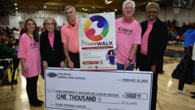 Five people posing for a photo holding a giant check on a high school basketball court