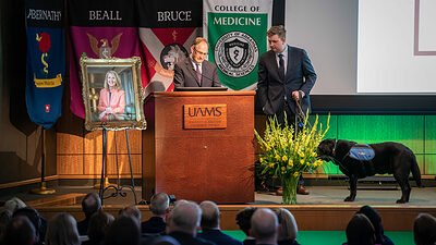 Andrew Morris, Ph.D., addresses the crowd, flanked by his late wife's portrait and son Edward, as well as the family dogs Saleh and Carmine.