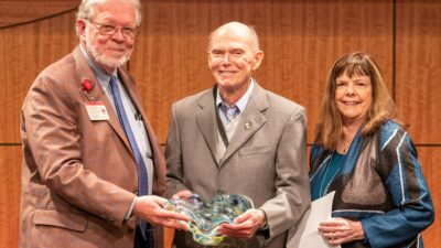 David L. Davies, Ph.D., a professor in the Department of Neurobiology and Developmental Sciences (center) is the UAMS College of Medicine's 2023 Distinguished Faculty Service Award winner. He is joined on stage by Interim Dean and UAMS Executive Vice Chancellor G. Richard Smith, M.D., (left) and his nominator, Gwen Childs, Ph.D., chair of Neurobiology and Developmental Sciences.