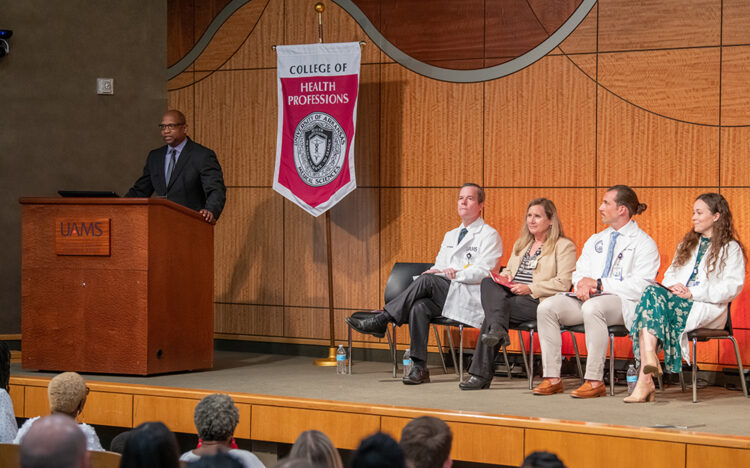 Edwards Williams, left, speaks at the start of the white coat ceremony for physician assistant students. The speakers seated are Chancellor Cam Patterson, left, Dean Susan Long, Ryan Toliver and Ada Sochanska.