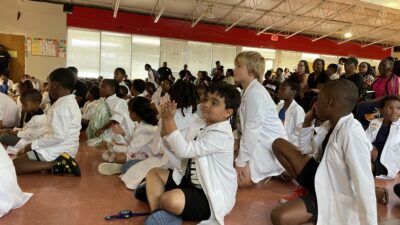 Children from Pathways Academy watch as their fellow students perform STEM-themed songs during a closing ceremony for summer programs at Carver STEAM Magnet Elementary School in Little Rock.