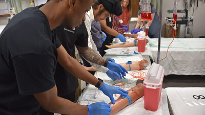 Students in the Pre-Nursing Summer Scholars program use manikin arms to practice blood-draw techniques.